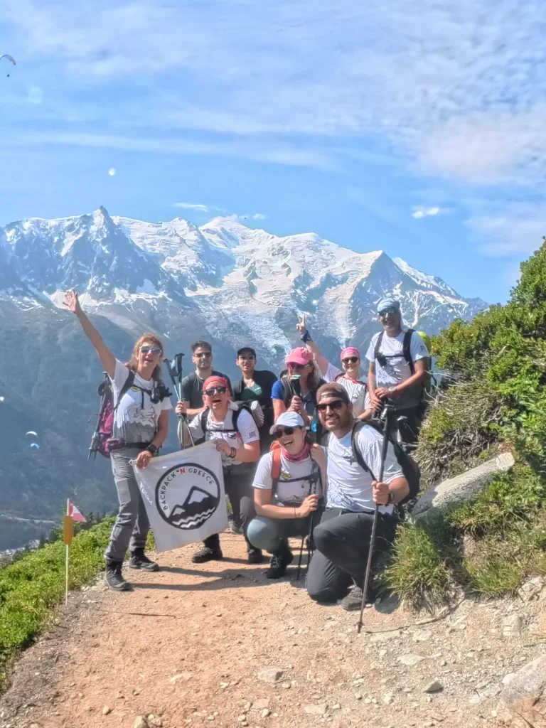 Tour du Mont Blanc Vol.3, η ομάδα ποζάρει σε αλπικό μονοπάτι με χιονισμένο ορεινό όγκο στο φόντο.