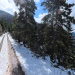 Στάση για μια ματιά πίσω, εκεί που η διαδρομή συναντά τη θέα. Χιονισμένος ορεινός δρόμος στο Μαίναλο με θέα σε δάσος και βουνά