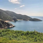 Μικροί κρυμμένοι όρμοι και δρόμοι που σε οδηγούν πάντα πιο κοντά στη θάλασσα. Παραθαλάσσια διαδρομή στη Μέσα Μάνη με μικρό όρμο και γαλήνια νερά κάτω από ανοιξιάτικο ουρανό