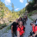 Η διαδρομή συνεχίζεται με χαλαρό ρυθμό, σε ανοιχτό κομμάτι με θέα και φως. Ομάδα πεζοπόρων σε χωμάτινο μονοπάτι δίπλα στο φαράγγι με θέα στη βλάστηση της περιοχής