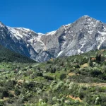 Εντυπωσιακή θέα προς τον Χελμό, με τις χιονισμένες κορυφές να υψώνονται πάνω από το καταπράσινο τοπίο. Η Λίμνη Τσιβλού και οι κορυφές του Χελμού σε ανοιξιάτικο τοπίο