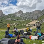Μια ανάσα στο αλπικό λιβάδι η ομάδα ξεκουράζεται σε αλπικό λιβάδι με αγριολούλουδα, δίπλα στο μονοπάτι και με βραχώδεις κορυφές στο φόντο