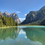 Καθρέφτες βουνών πάνω στο νερό ορεινή λίμνη με γαλαζοπράσινα νερά, πυκνά δάση και απότομες βραχώδεις πλαγιές να καθρεφτίζονται στην επιφάνειά της