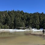 Ρομαντική στιγμή με φόντο τη λίμνη και τα χιονισμένα έλατα. Ζευγάρι δίπλα στην εποχιακή λίμνη στον Παρνασσό